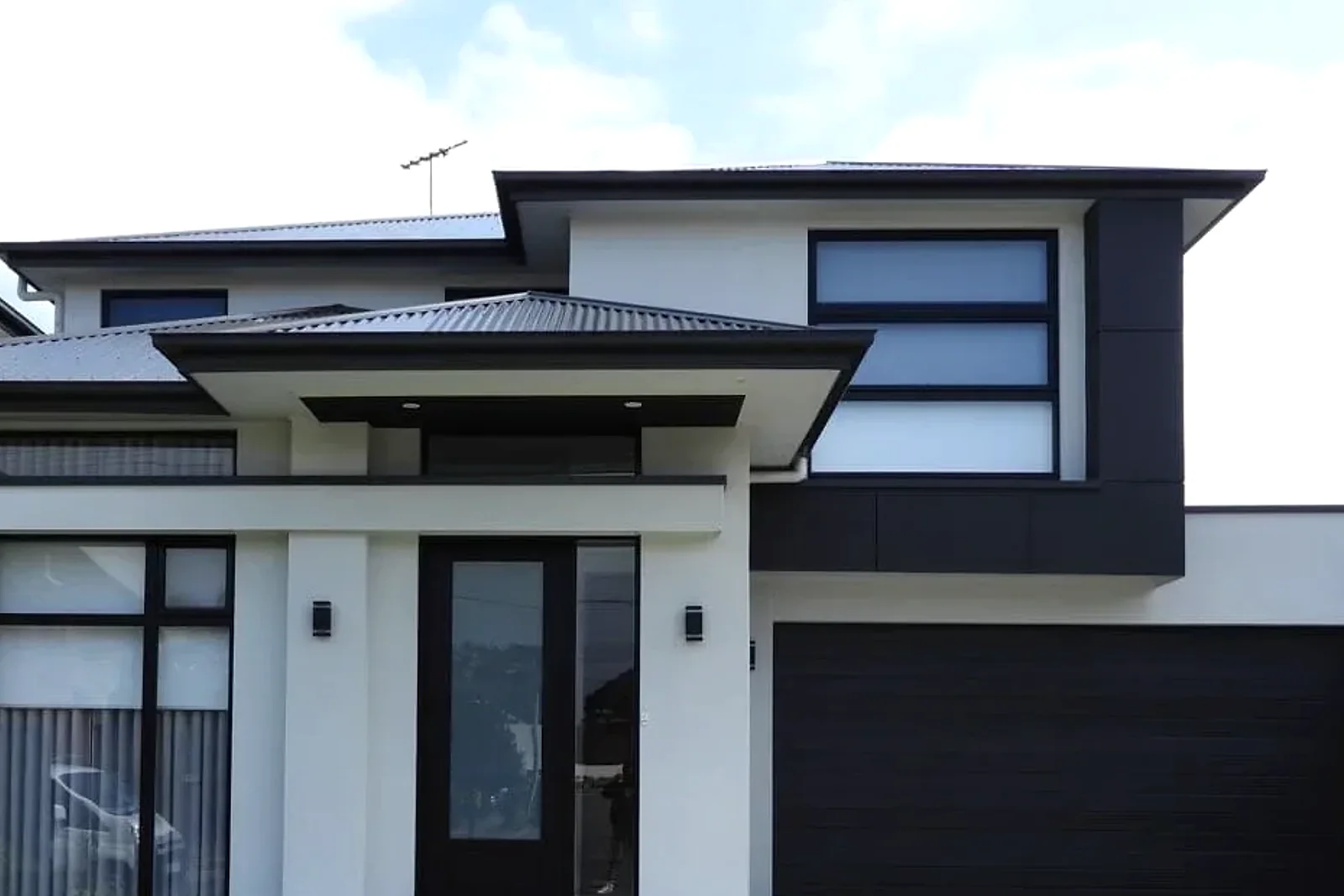 Two-storey residence with dark panel cladding around an upper window and garage projection