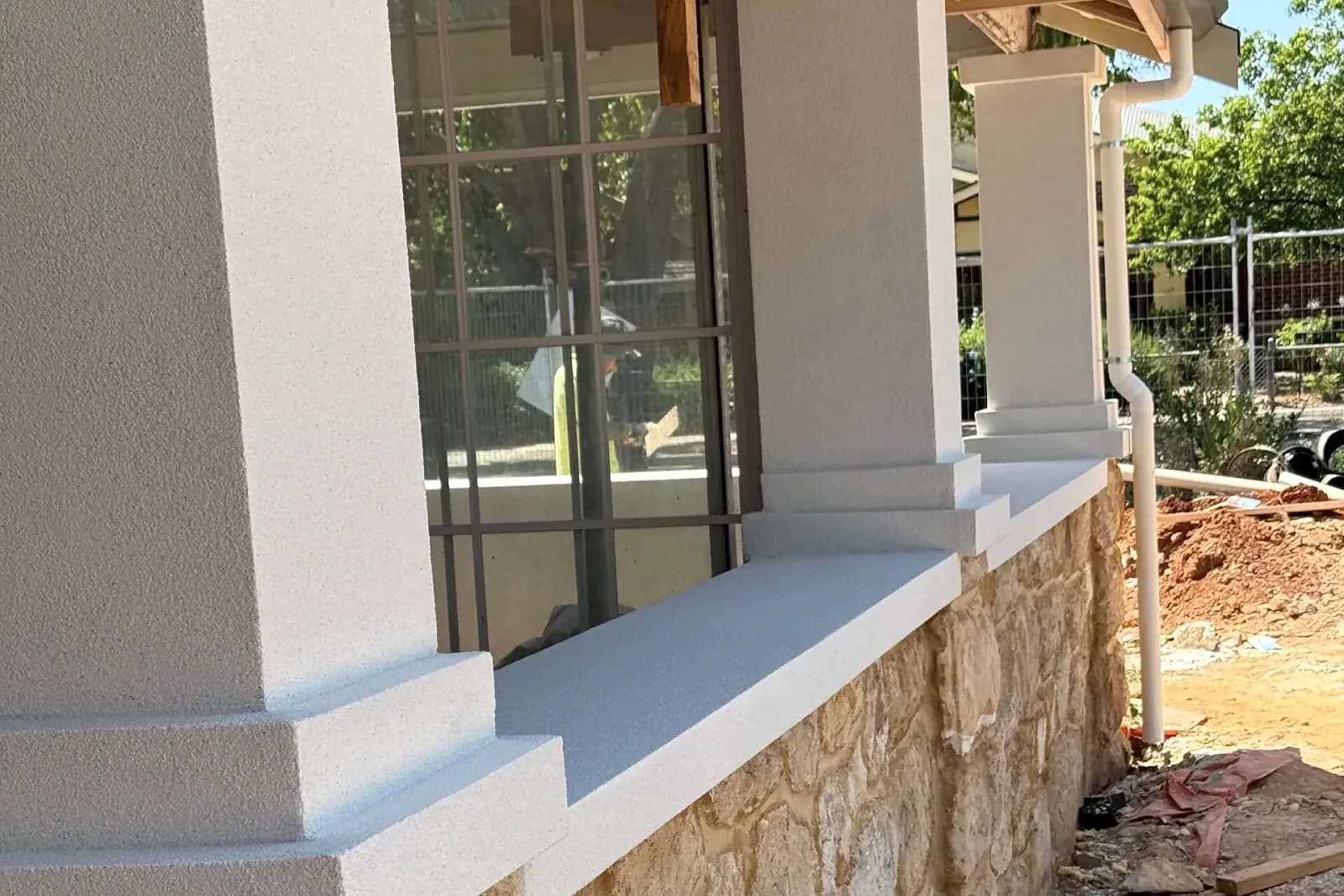 Textured rendered columns and ledges meeting a stone-faced base during exterior works